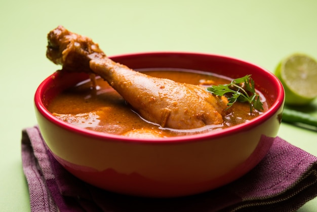 Poulet au curry rougeâtre épicé ou masala, avec un morceau de cuisse proéminent, servi dans un bol ou un kadhai sur fond coloré ou en bois. mise au point sélective.