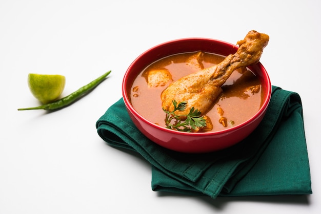 Poulet au curry rougeâtre épicé ou masala, avec un morceau de cuisse proéminent, servi dans un bol ou un kadhai sur fond coloré ou en bois. mise au point sélective.