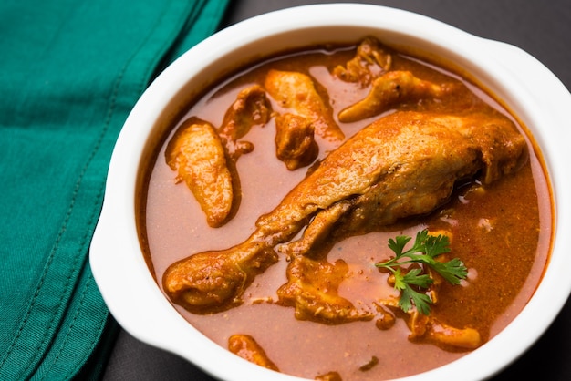 Poulet au curry rougeâtre épicé ou masala, avec un morceau de cuisse proéminent, servi dans un bol ou un kadhai sur fond coloré ou en bois. mise au point sélective.