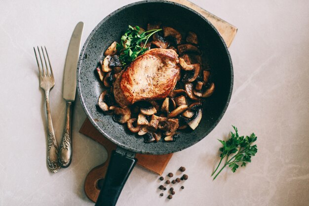 Poulet aux champignons dans une casserole se trouve sur un fond clair Déjeuner de poulet à côté de couverts vintage