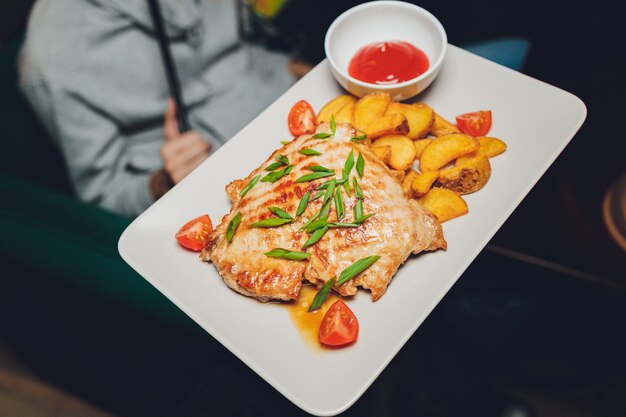 Poulet aux pommes de terre rôties sur une assiette blanche.