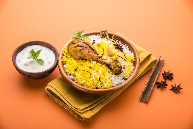 Poulet Biryani authentique servi dans un bol ou une assiette sur fond coloré ou en bois. C'est une délicieuse recette de riz basmati mélangé avec du poulet mariné épicé servi avec une salade. Mise au point sélective