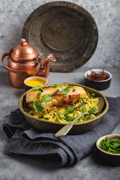 Poulet Biryani, plat traditionnel de la cuisine indienne, avec riz basmati, oignon frit, coriandre fraîche dans un bol sur fond de pierre rustique grise. Repas indien authentique, gros plan, mise au point sélective