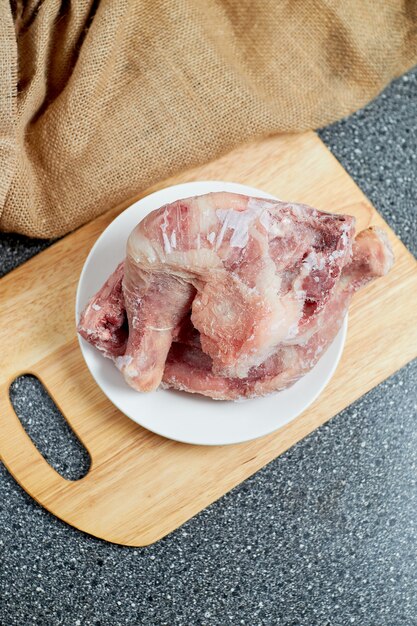 Photo poulet congelé se trouve sur une plaque blanche sur une planche de bois