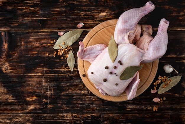 Poulet cru aux épices sur planche de bois sur fond de bois foncé.