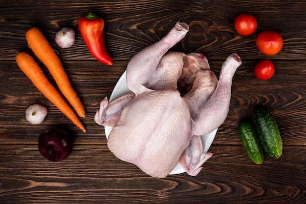 Poulet cru sur bois foncé avec des légumes.