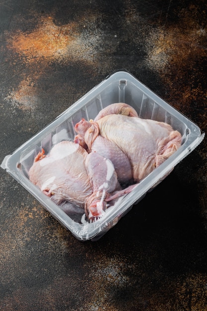 Poulet cru dans une boîte en plastique scellée en plastique, sur fond rustique ancien