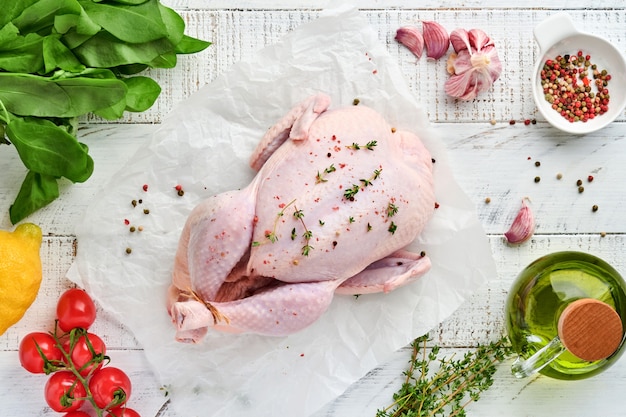 Poulet cru entier avec des ingrédients pour faire du poivre, du citron, du thym, de l'ail, de la tomate cerise, de l'oseille et du sel dans la cuisine sur fond gris clair en ardoise, pierre ou béton. Vue de dessus avec espace de copie.