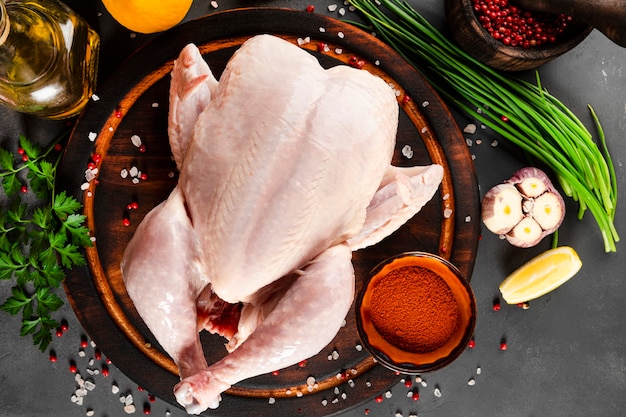 Poulet cru entier sur la planche à découper en bois et assaisonnements pour la cuisson vue de dessus, espace libre pour le texte. Fond gris foncé. photo de haute qualité