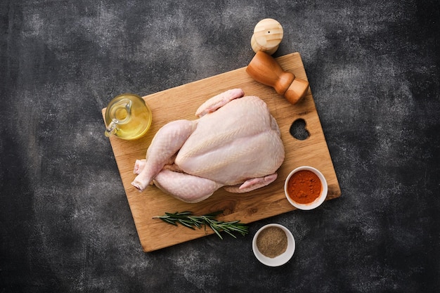 Un poulet cru entier reposant sur une planche de bois sur un fond sombre Préparation du poulet cru Vue de dessus