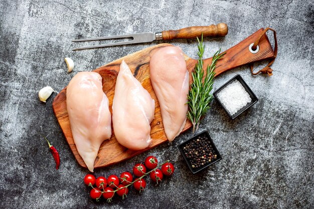 Poulet cru sur une planche à découper avec des épices et des herbes.