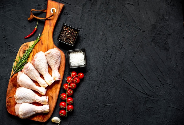 Poulet cru sur une planche à découper avec des ingrédients sur fond noir.