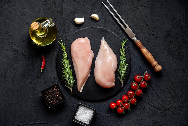 Poulet cru sur une table en pierre noire avec des épices et des herbes.