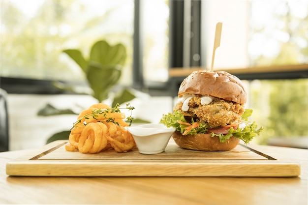 Poulet cuit savoureux avec sauce à la roquette et mayonnaise servi sur planche de bois, poulet cuit Burger au fromage avec frites frisées assaisonnées épicées