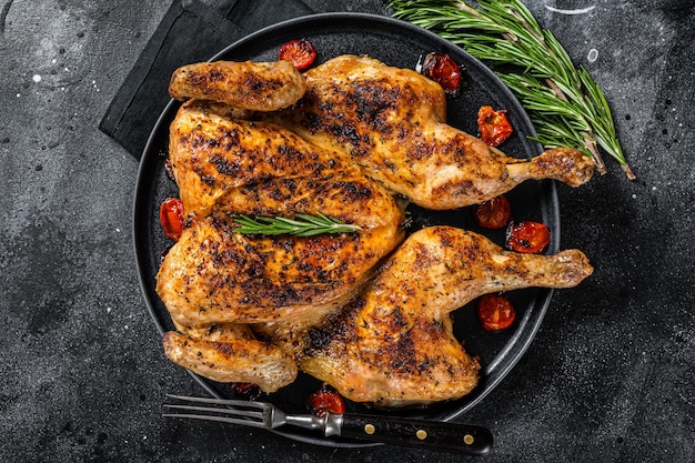 Poulet entier au tabac sur assiette avec herbes et tomate Fond noir Vue de dessus