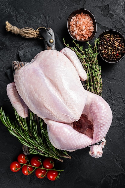 Poulet entier cru non cuit sur planche de bois avec thym et romarin Fond noir Vue de dessus