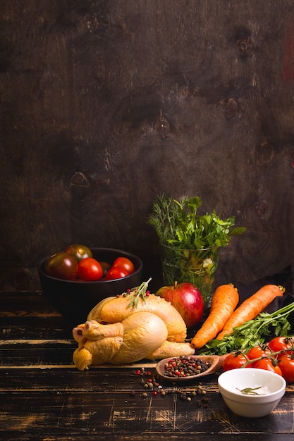 Poulet entier cru prêt pour la cuisson. Poulet, légumes, herbes, épices sur fond de bois rustique