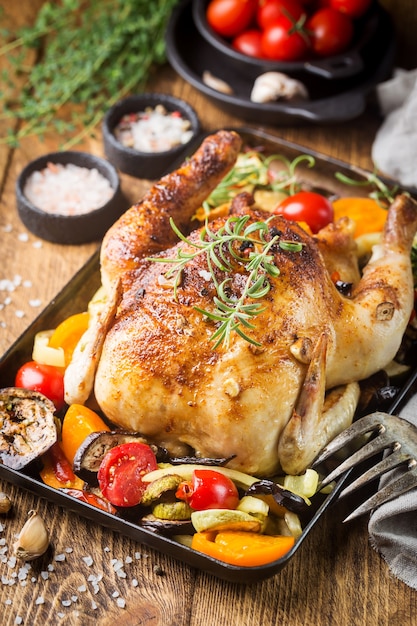 Poulet entier cuit au four avec gros plan de légumes et d'herbes sur une assiette sur une table.