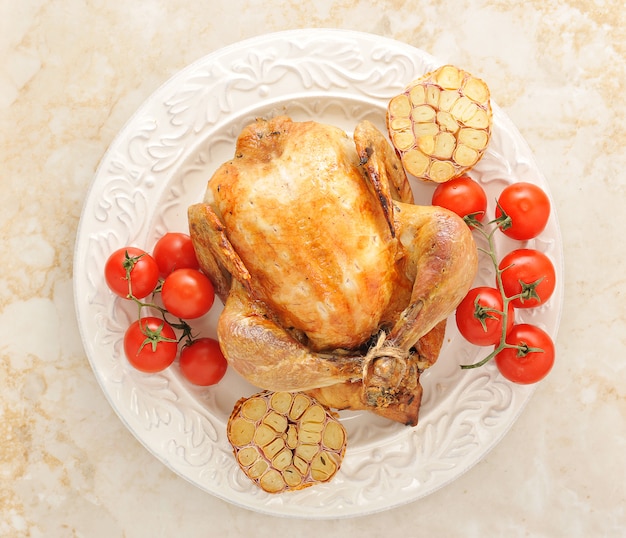 Poulet entier grillé sur une assiette avec des tomates et de l'ail