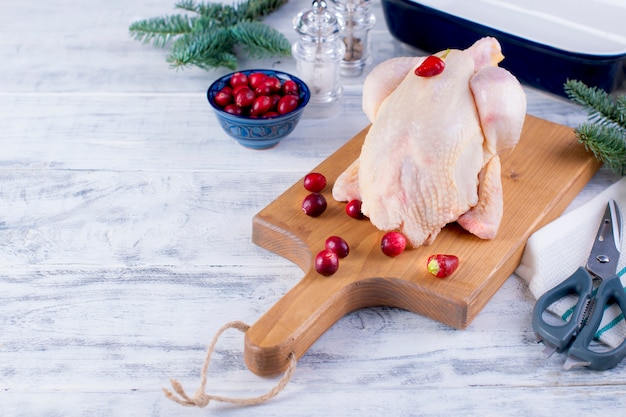 Poulet frais sur une planche de bois avec des fruits rouges et des branches d'épinette