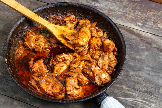 Poulet frit aux épices dans une poêle avec une spatule en bois sur une table sombre