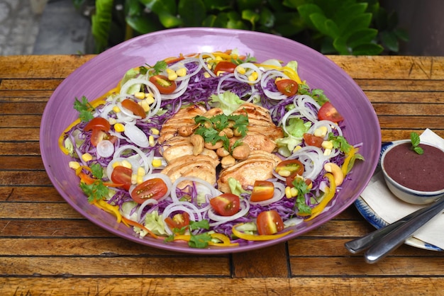 Poulet frit à la poêle sur une assiette violette avec des légumes verts et de la sauce aux mûres sur une table en bois