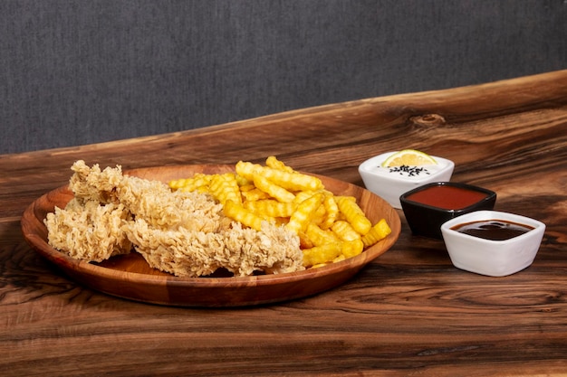 Photo poulet frit avec des pommes de terre frites dans une assiette à côté d'une variété de sauces et d'épices sur un plateau en bois