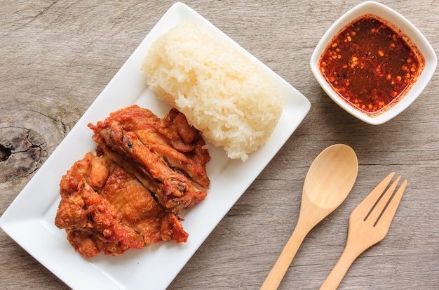 Poulet frit style thaï avec sauce épicée rouge et riz gluant isolé sur une table en bois