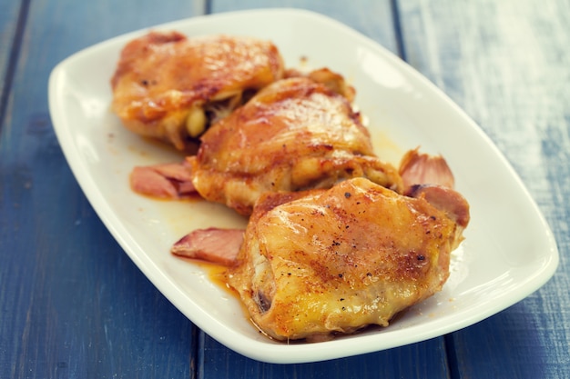 Poulet frit avec de la viande fumée sur une plaque blanche sur bois