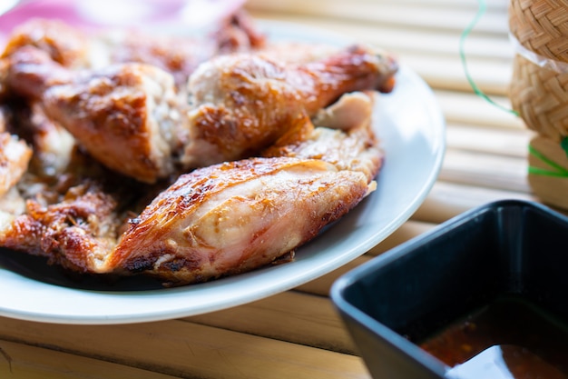 Photo poulet grillé haché en morceaux, posé sur une assiette sur une table en bambou avec une sauce moyennement épicée.
