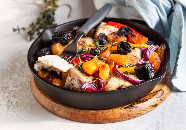 Photo poulet grillé avec légumes et fruits secs dans une poêle en fonte.