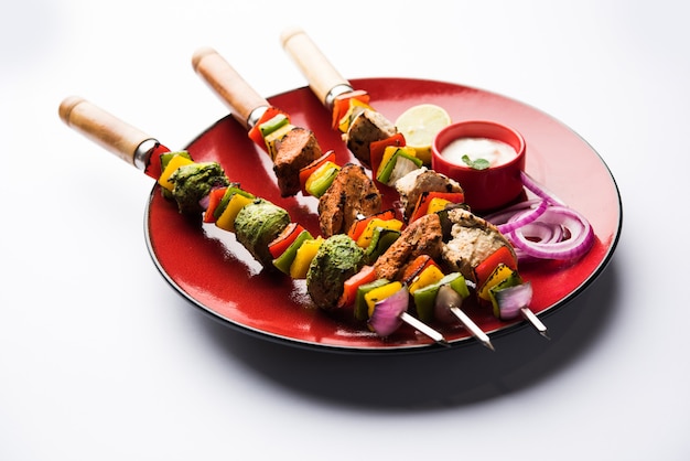 Poulet Hariyali kakab ou Malai malai kebab en tricolore servi avec des brochettes et une trempette au yaourt dans une assiette