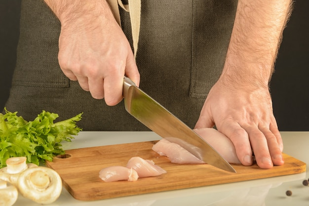 Poulet. Un homme en tablier coupe de la viande sur une planche de bois.