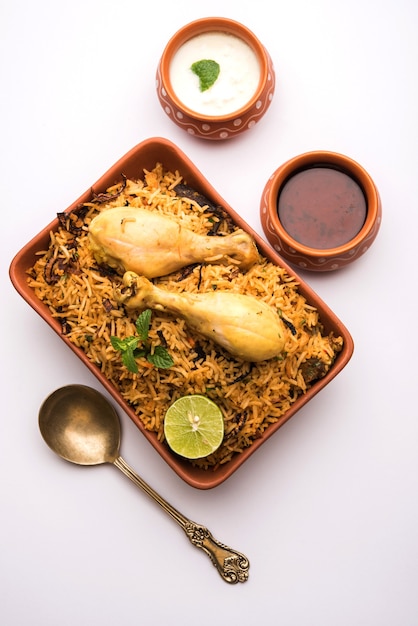 Poulet indien Biryani servi dans un bol en terre cuite avec du yaourt sur fond blanc. mise au point sélective