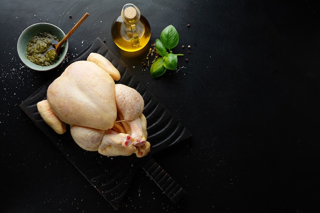 Poulet de maïs entier cru avec des épices sur table sombre