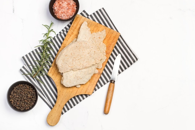 Poulet milanais sur une planche de cuisine en bois sur un comptoir de cuisine en marbre blanc en vue de dessus