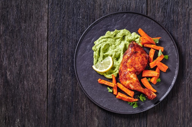 Photo poulet rôti avec sauce guasacaca de poivre vert avocat et herbes et chips de patate douce sur plaque noire sur table en bois vue horizontale d'en haut espace libre à plat