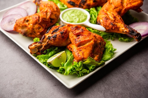 Le poulet tandoori est un plat de poulet préparé en rôtissant du poulet mariné dans du yaourt et des épices dans un tandoor ou un four d'argile, servi avec de l'oignon et du chutney vert