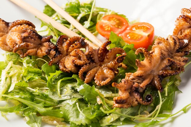 Poulpe bébé barbecue sur une plaque blanche avec des herbes, des tomates et des bâtons