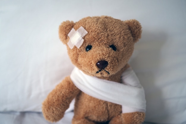 Poupée ours triste malade au lit avec la plaie à la tête et un bandage