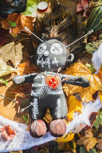 poupée vaudou percée d'aiguilles se trouve sur une table avec des feuilles mortes et des citrouilles