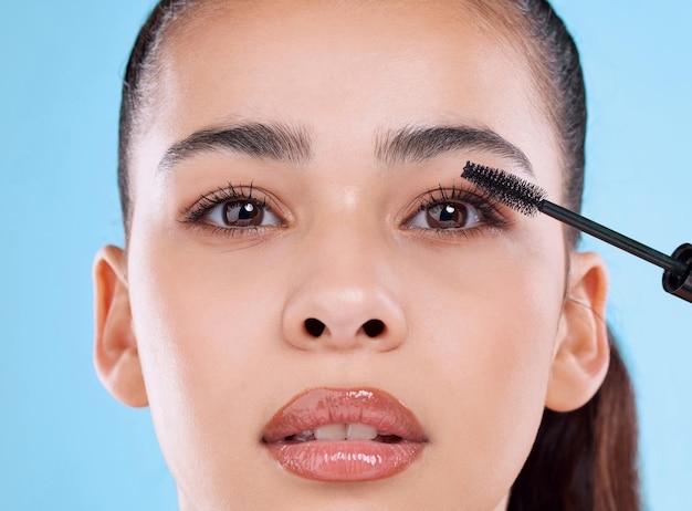 Pour des cils plus longs Portrait en studio d'une jolie jeune femme appliquant du mascara sur fond bleu