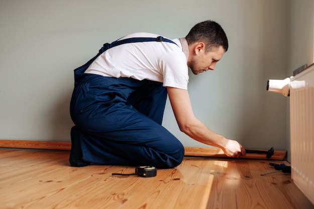 Pour faire des réparations. Pose d'une nouvelle plinthe. un homme fait des réparations dans une pièce