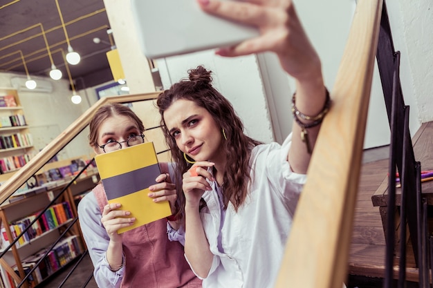 Pour une fausse image. Heureux les jeunes femmes se photographiant et posant avec un livre et avec des visages mignons