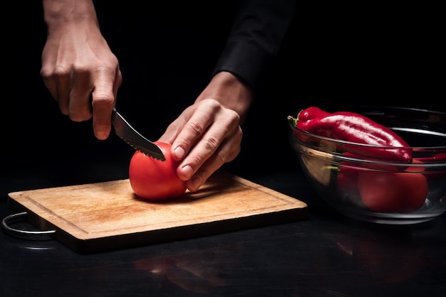 Pour un plat. Gros plan du jeune chef mans mains hacher la tomate pendant la cuisson et préparer les légumes pour la salade au restaurant.