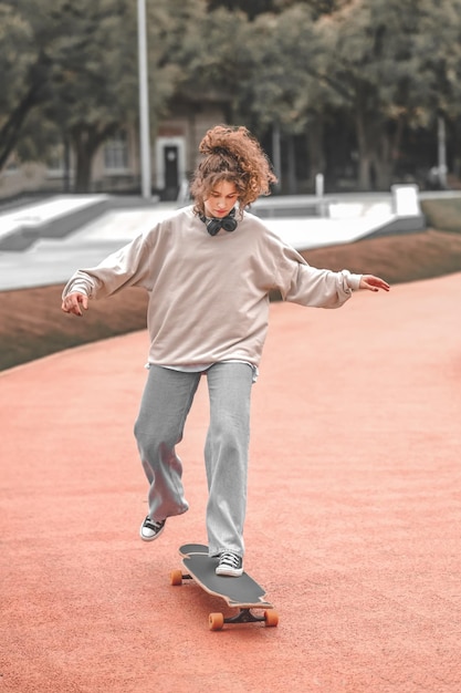 Pousser. Fille en jeans et baskets en sweat-shirt regardant attentivement debout sur une planche à roulettes poussant avec le pied dans le parc pendant la journée