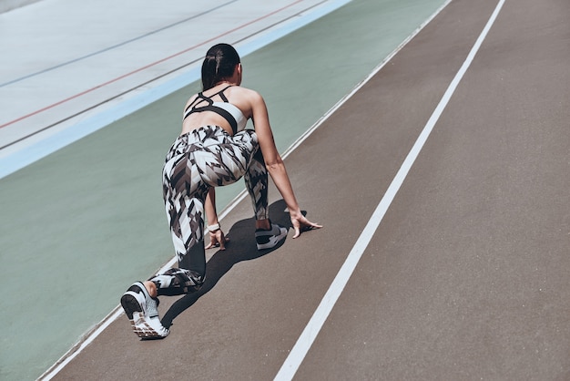 pousser fort. Vue arrière supérieure de la jeune femme en vêtements de sport debout sur la ligne de départ