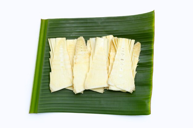 Pousses de bambou brutes tranchées sur feuille de bananier sur fond blanc.