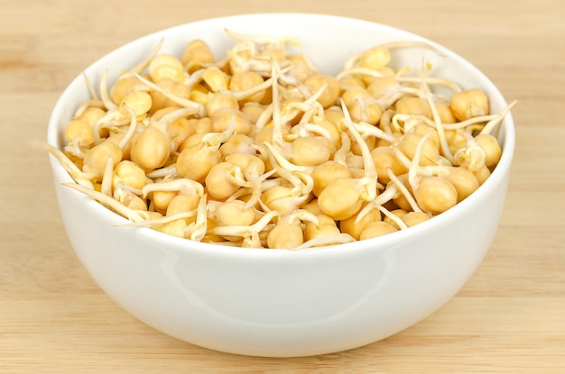 Pousses de pois chiches dans un bol blanc sur planche de bois