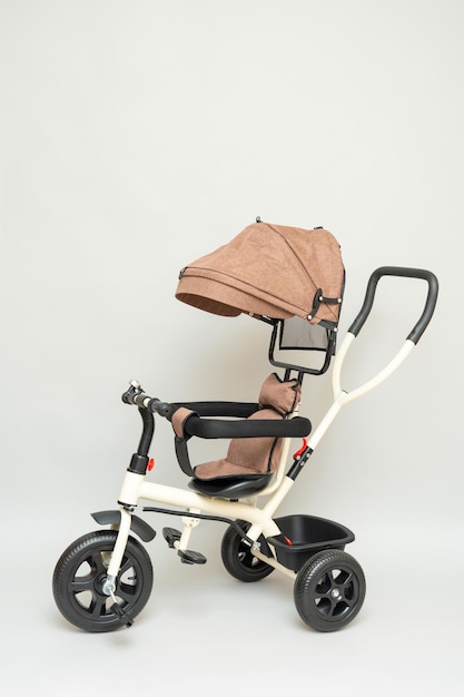 Poussette à trois roues pour enfants moderne beige avec une poignée pour le contrôle et des pédales sur fond gris